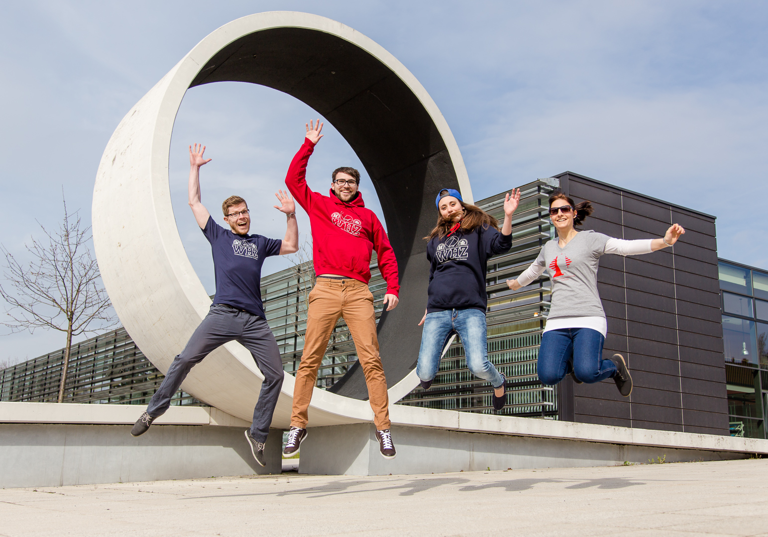 Foto: Vier Studierende und Shirts mit WHZ-Logos springen vor einem Betonelement in Form eines Loopings. 
