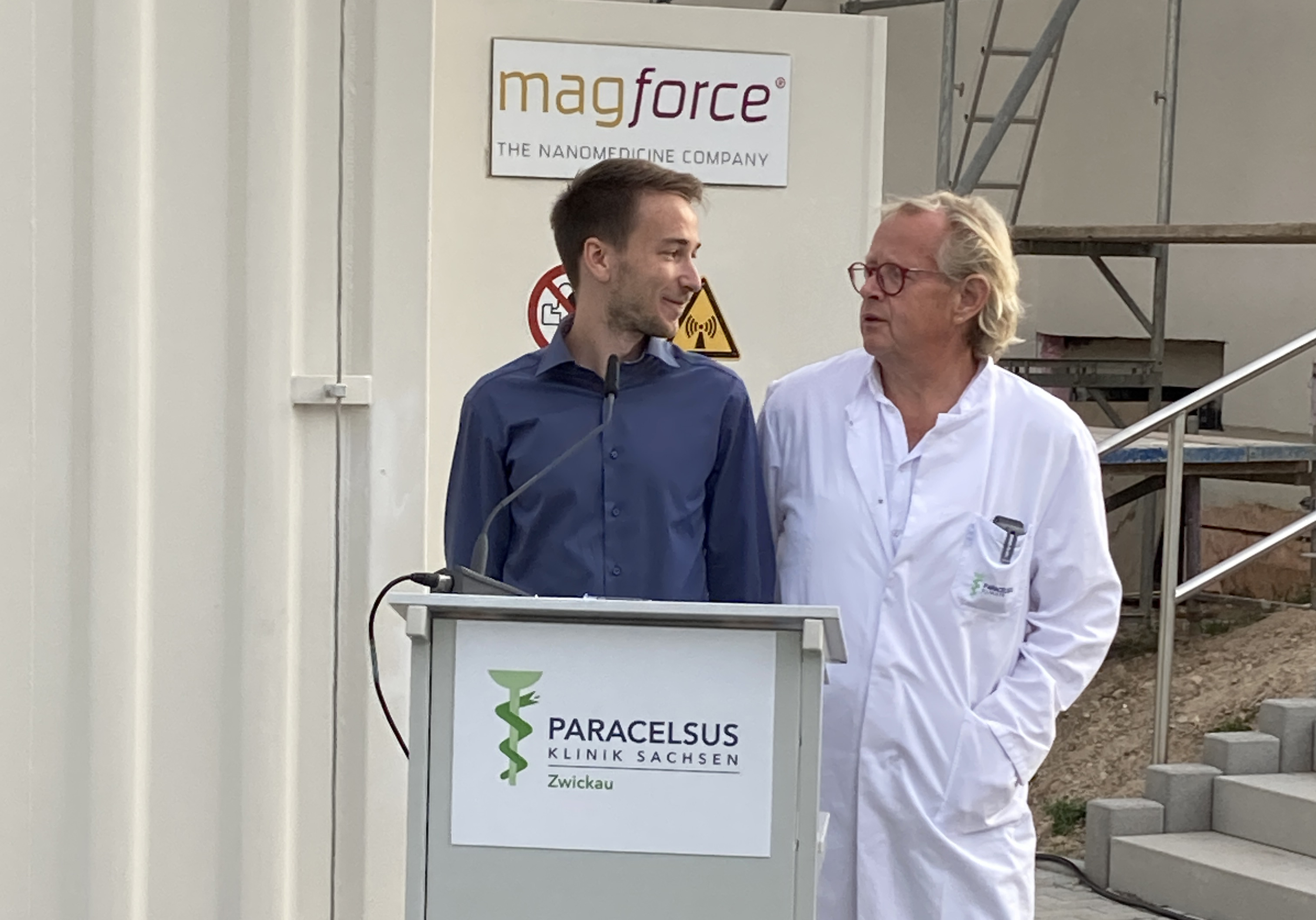 Foto: Luke Drechsler und Prof. Dr. Jan-Peter Warnke stehen an einem Rednerpult. Beide blicken sich freundschaftlich an. 