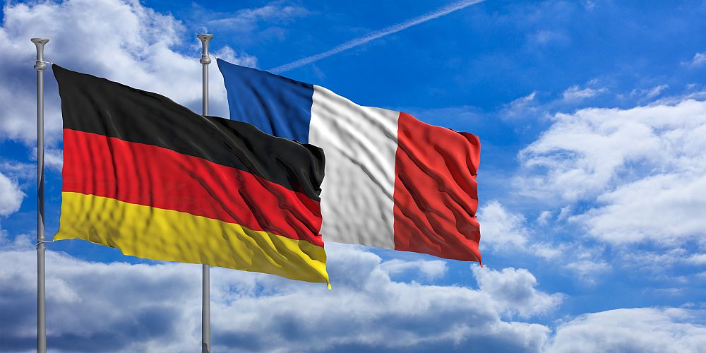 Foto: Vor blauem Himmel wehen eine deutsche und eine französische Fahne. 
