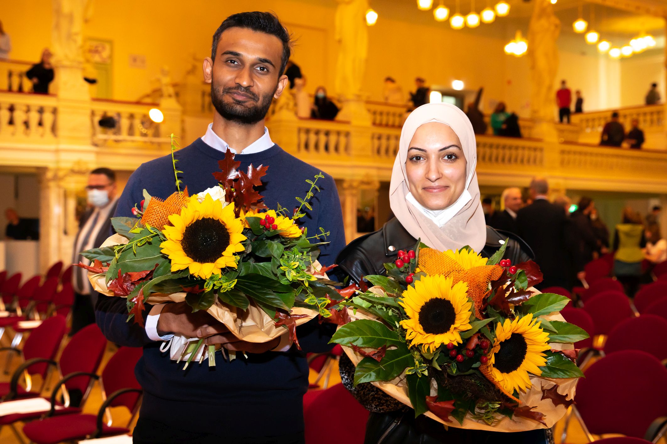 Foto: Ein Junger Mann und eine junge Frau stehen vor dem festlichen Saal der Zwickauer Neuen Welt und haben beide einen großen Blumenstrauß vor sich.