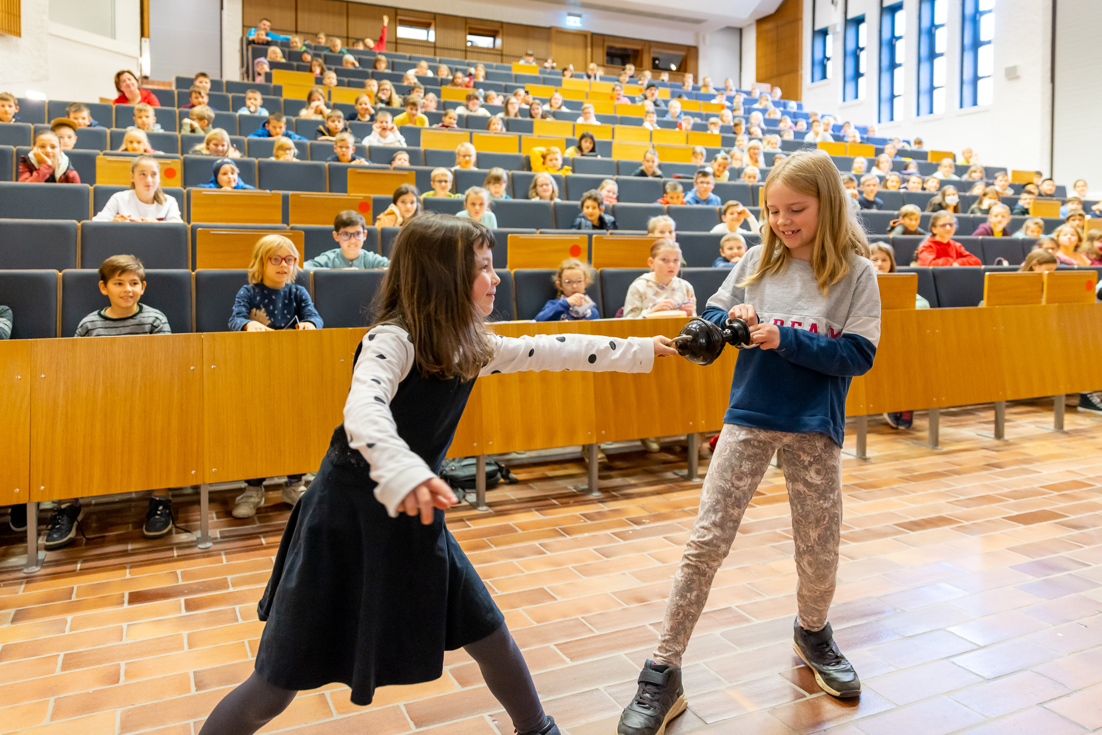 Zwei Mädchen bei dem Experiment "Magdeburger Halbkugeln" - im Hintergrund der volle Hörsaal