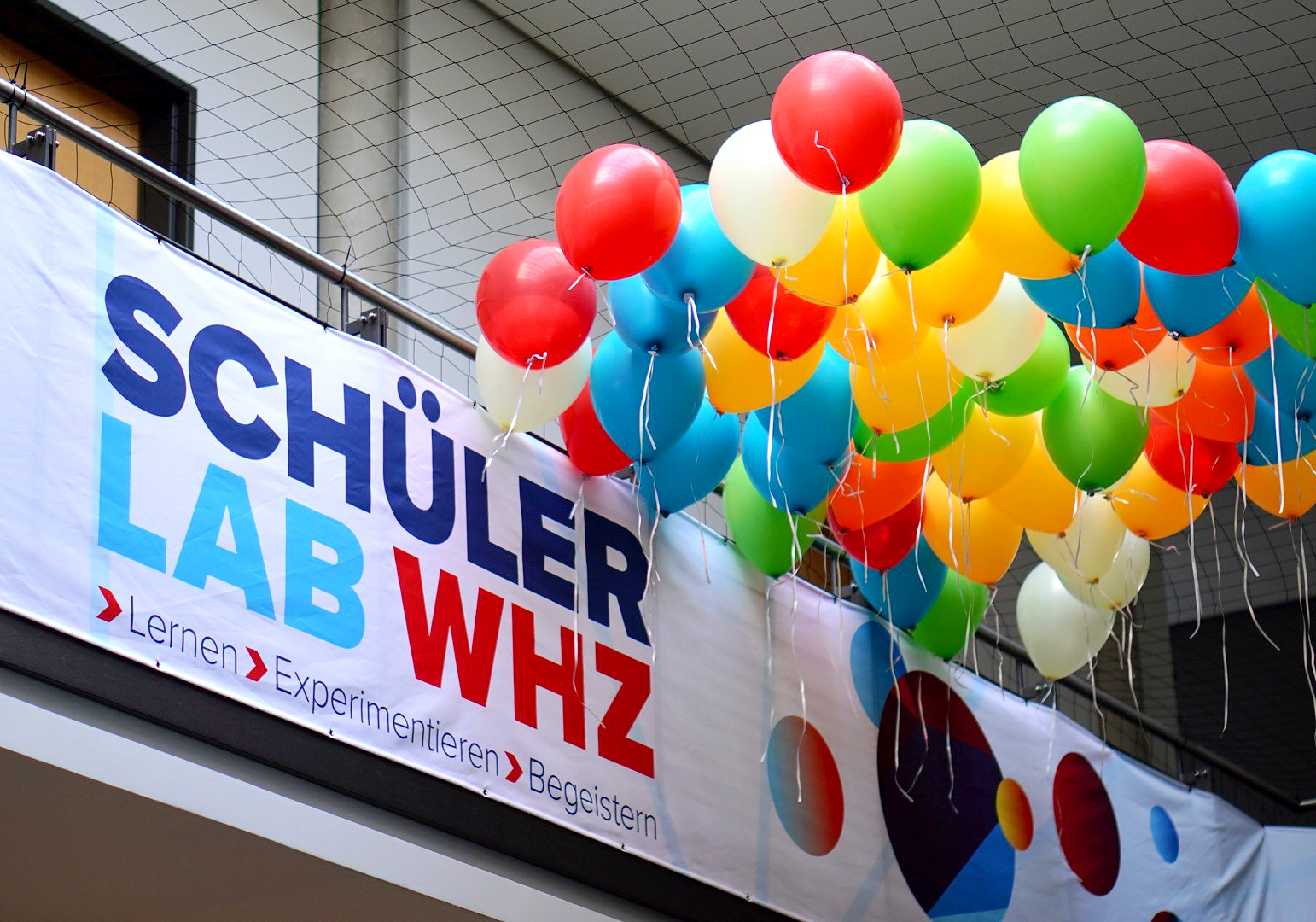 Ein Banner mit der Schrift SchülerLAB WHZ, darüber fliegen bunte Luftballons