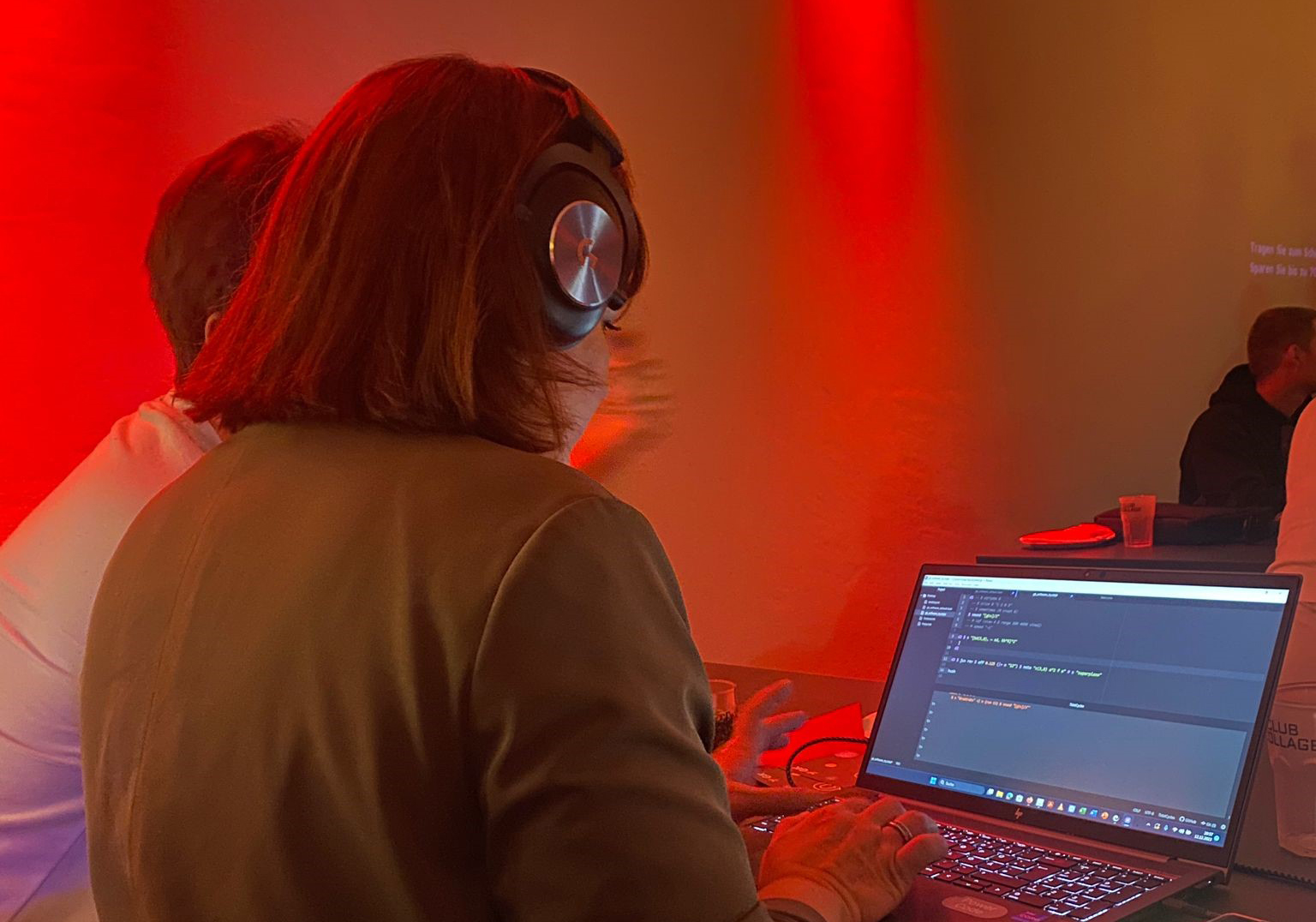 Eine Frau steht mit Kopfhörern an einem Laptop, im Hintergrund Diskolicht