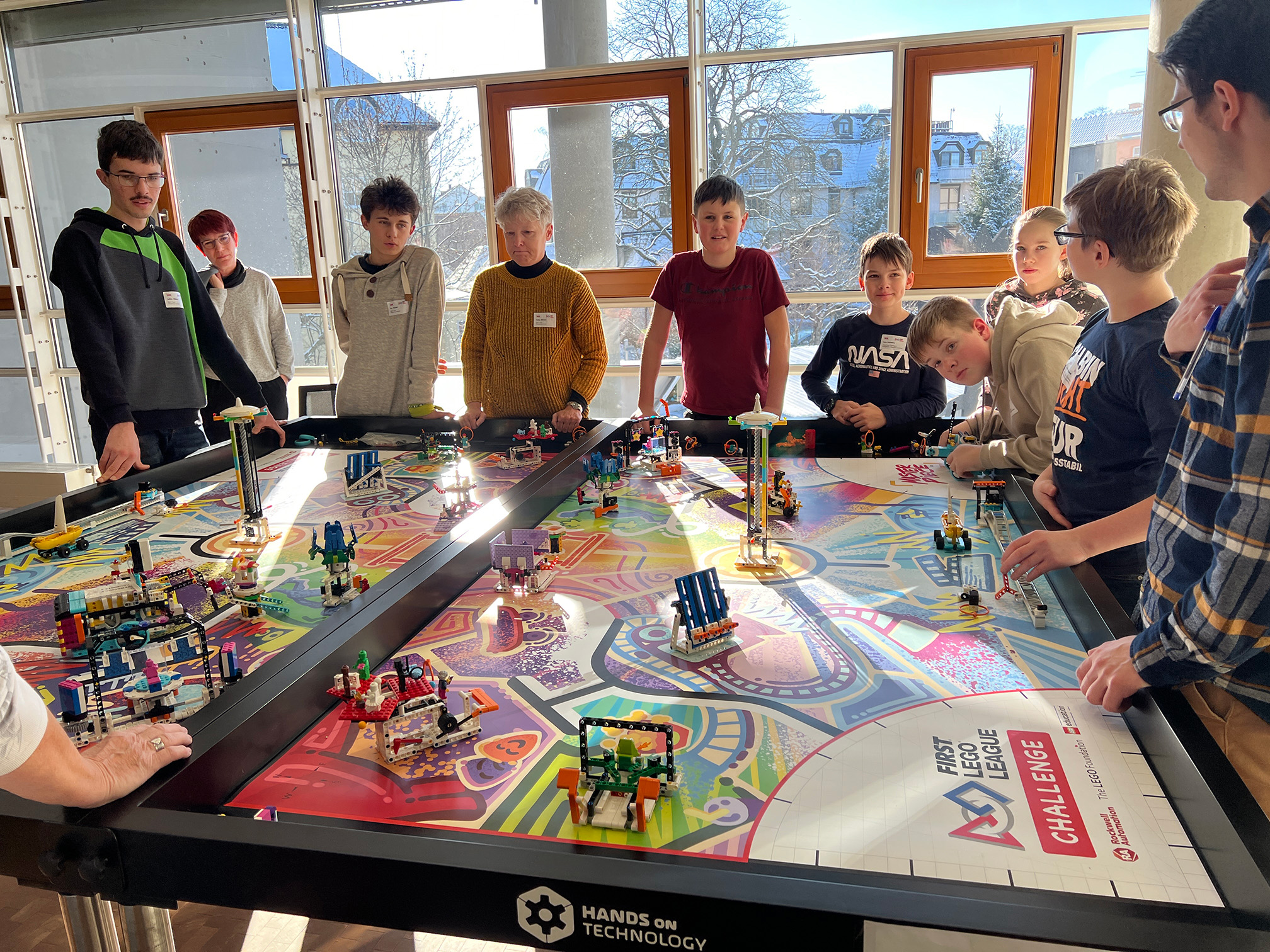 Schüler und Lehrer stehen um einen Lego-Spieltisch