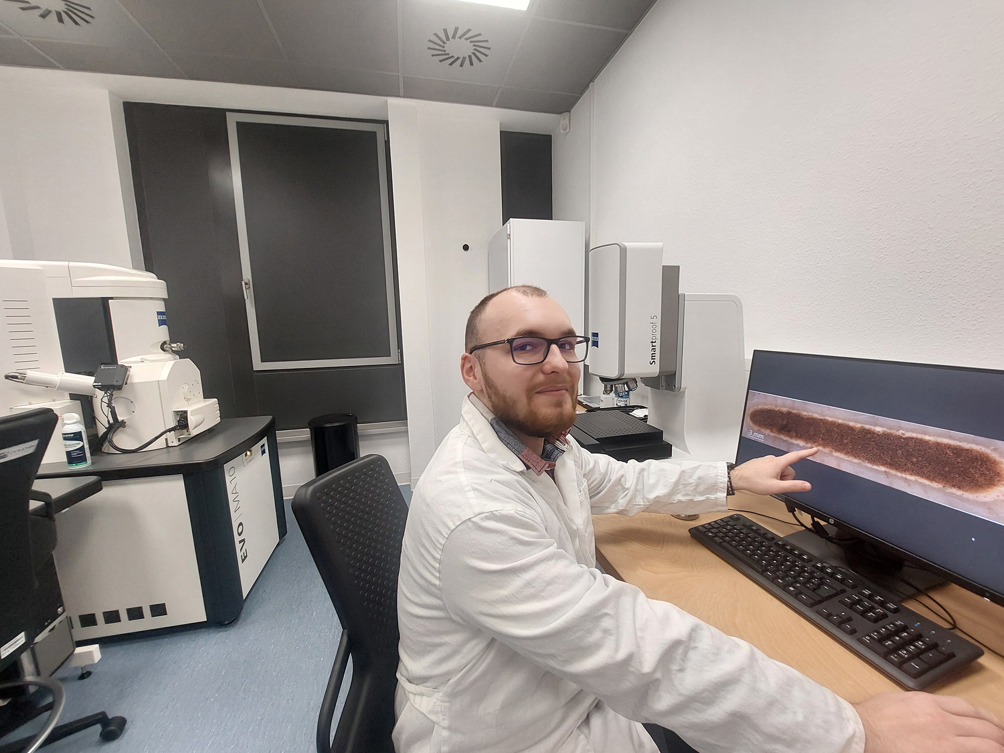 Wissenschaftler im Labor zeigt auf einen Bildschirm mit einer Mikroskopieaufnahme. 