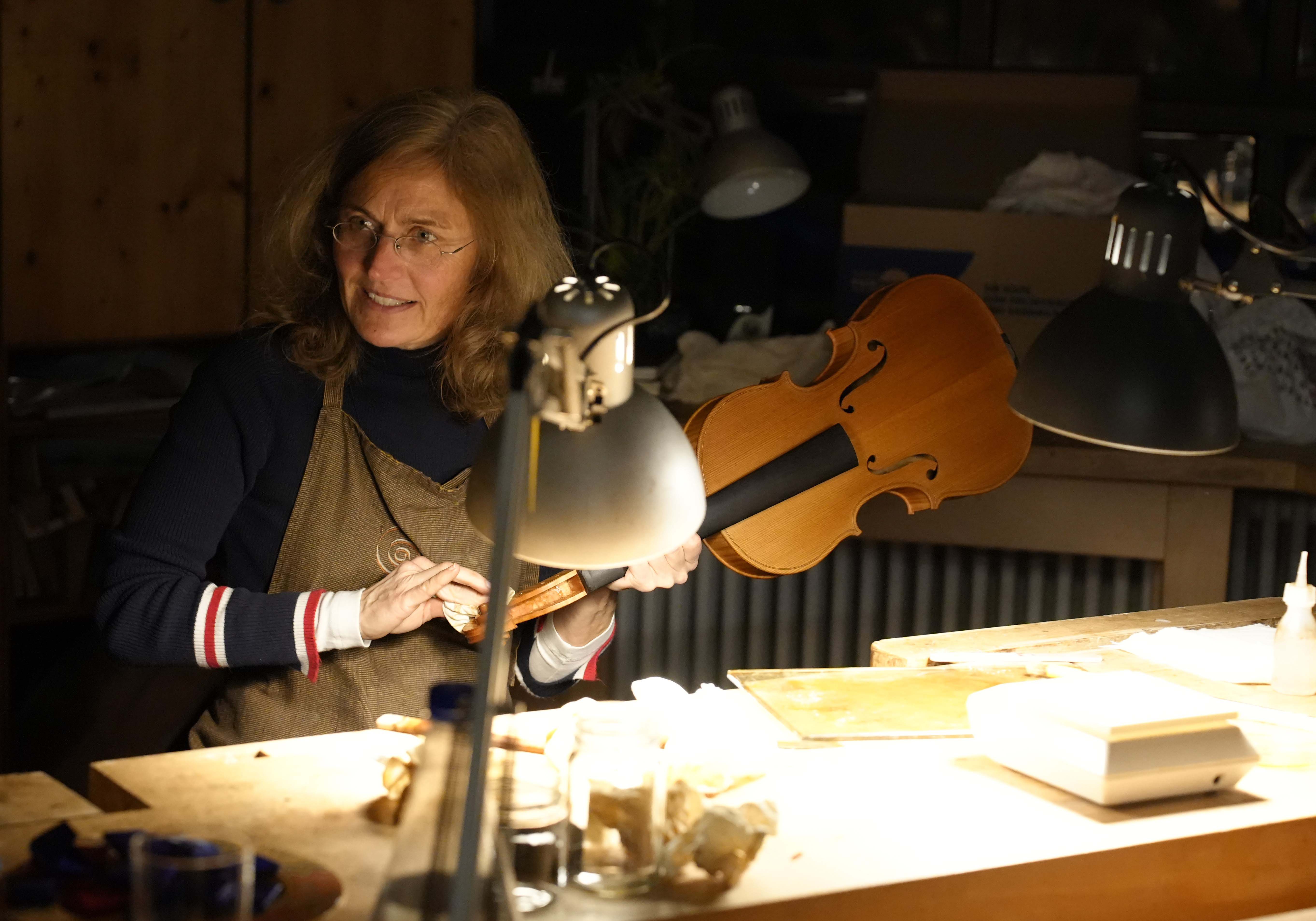Eine Frau sitzt in einer Werkstatt und arbeitet an einer Geige. 