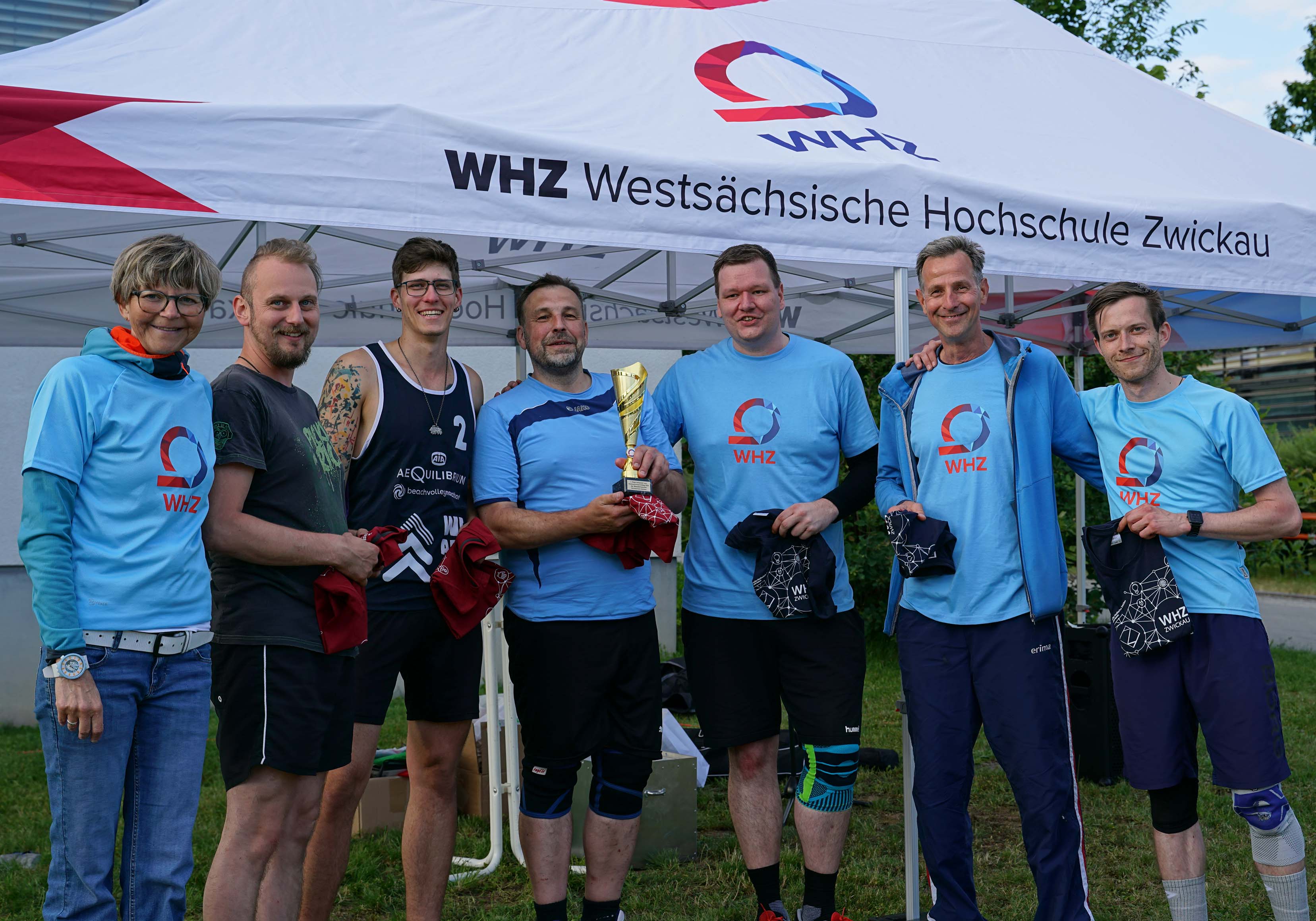 Gruppe aus Männern und Frauen in hellblauen T-Shirts der Hochschule zwickau hält Pokal als Sieger des Volleybalturniers in der Hand