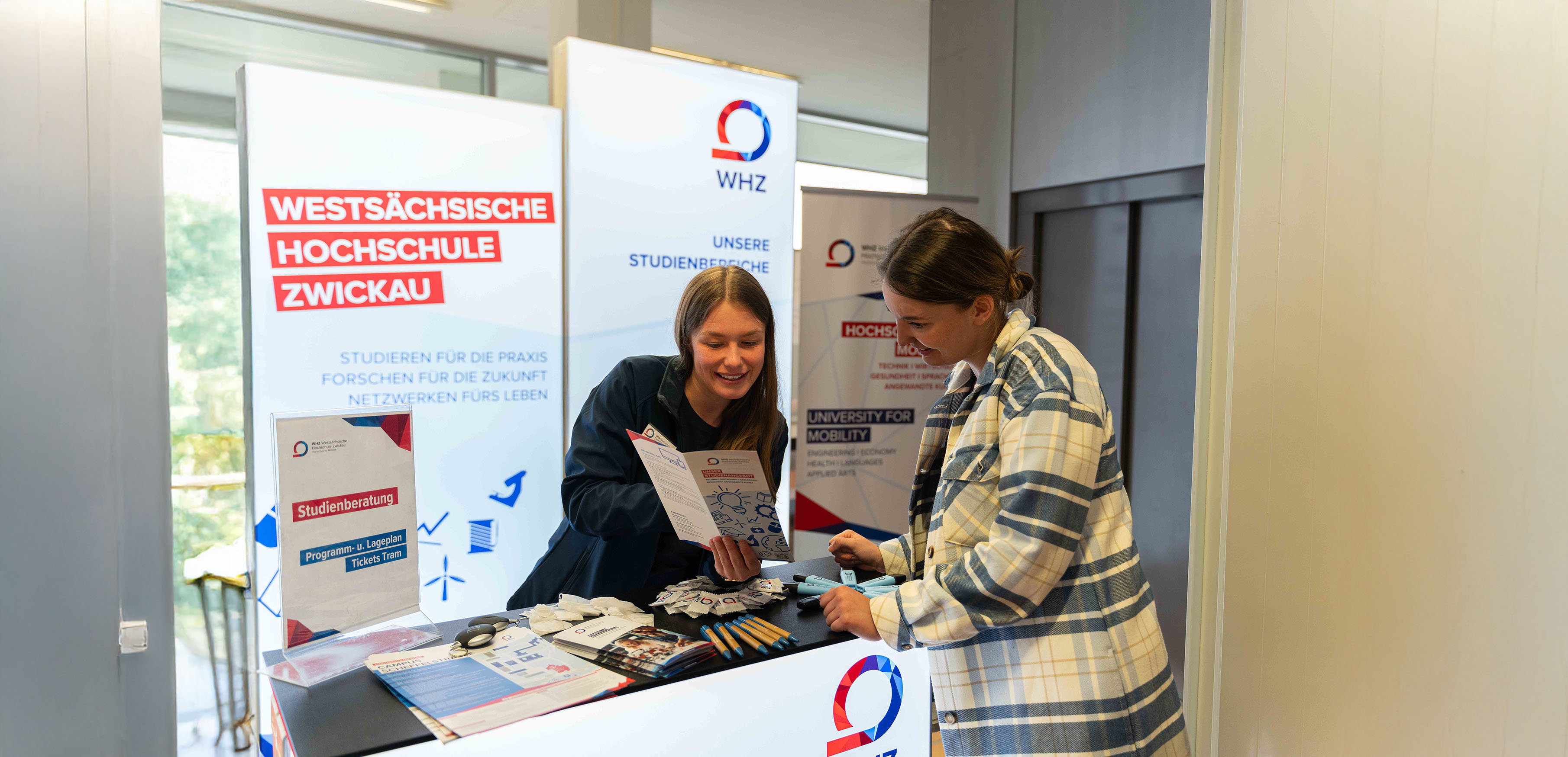 Eine Mitarbeiterin und eine Studentin unterhalten sich an einem Infostand der Hochschule. 