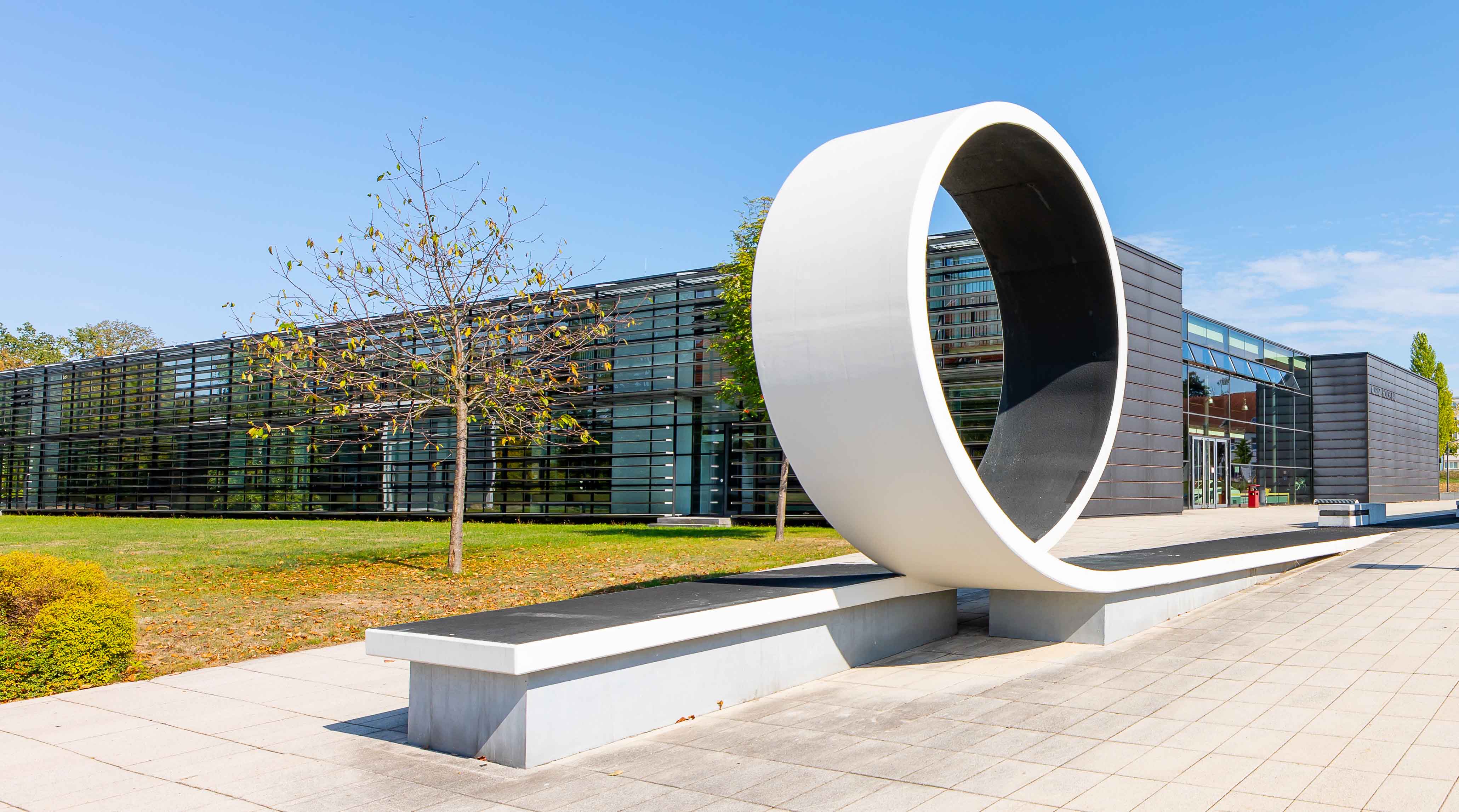 Foto: Campus Scheffelberg mit Blick auf das Laborgebäude Kraftfahrzeugtechnik / August-Horch-Bau. Davor eine Betonskulptur welche einen Looping zeigt.